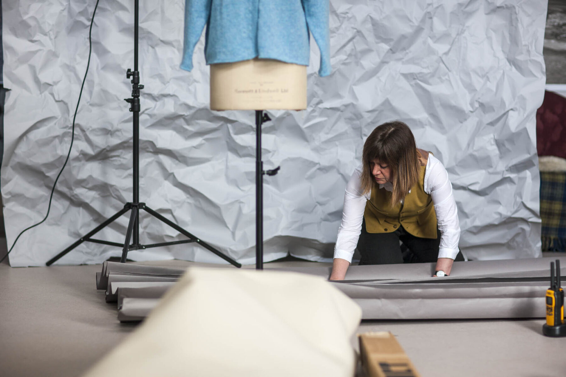 Gail folding paper backdrop for photo shoot. Tailors dummy in front of backdrop with blue knitwear.