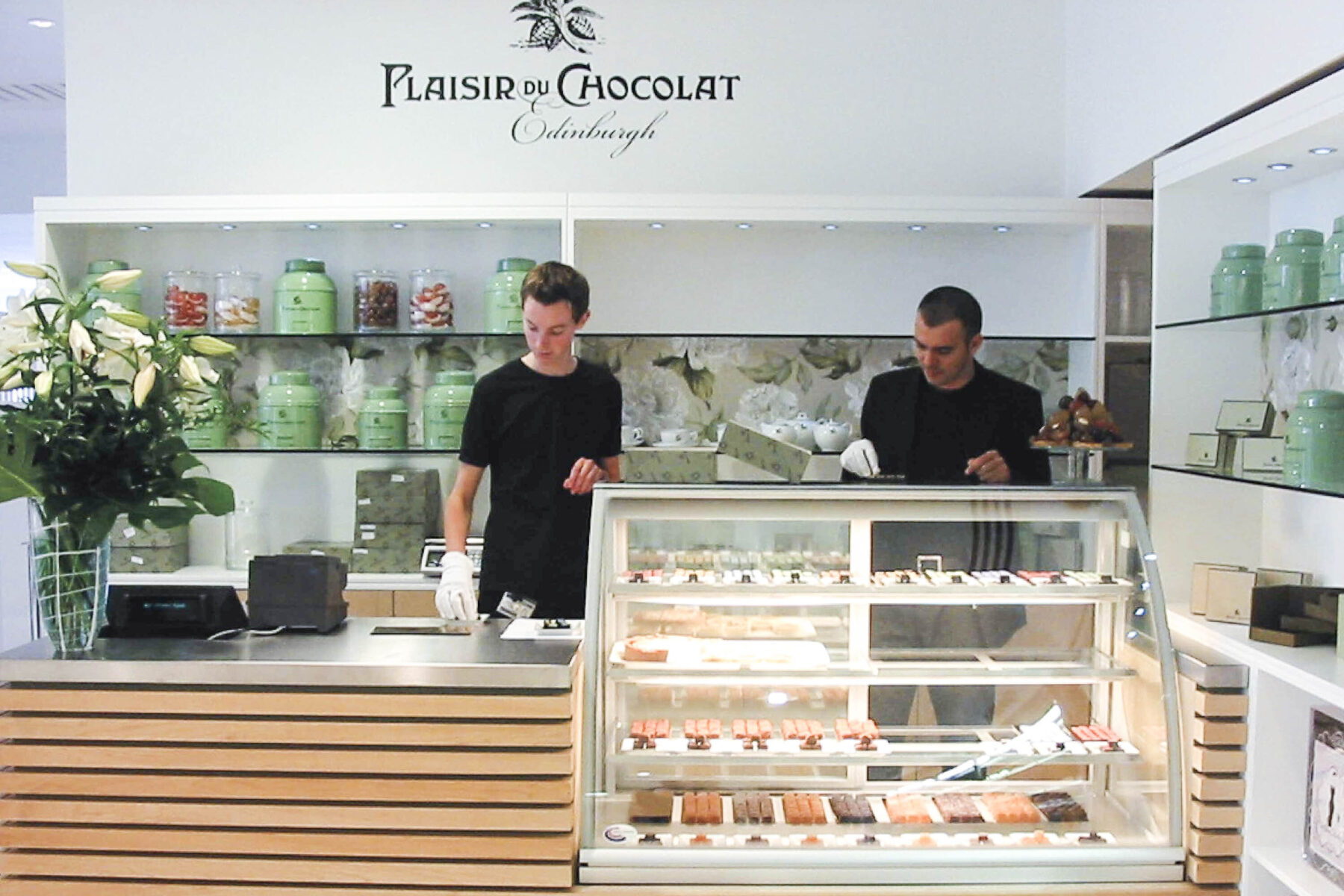 Plaisir du Chocolat shop within Harvey Nichols. 2 men at chiller cabinet with chocolates.