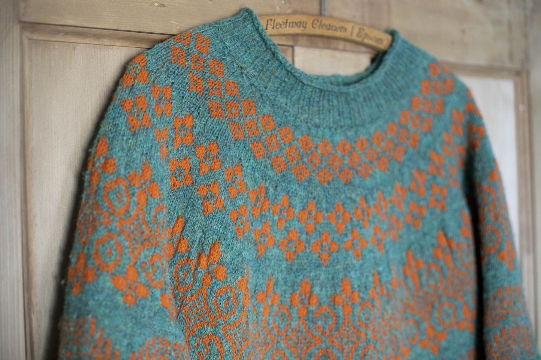 Green and orange hand knitted fairisle jumper hanging against a wooden door.