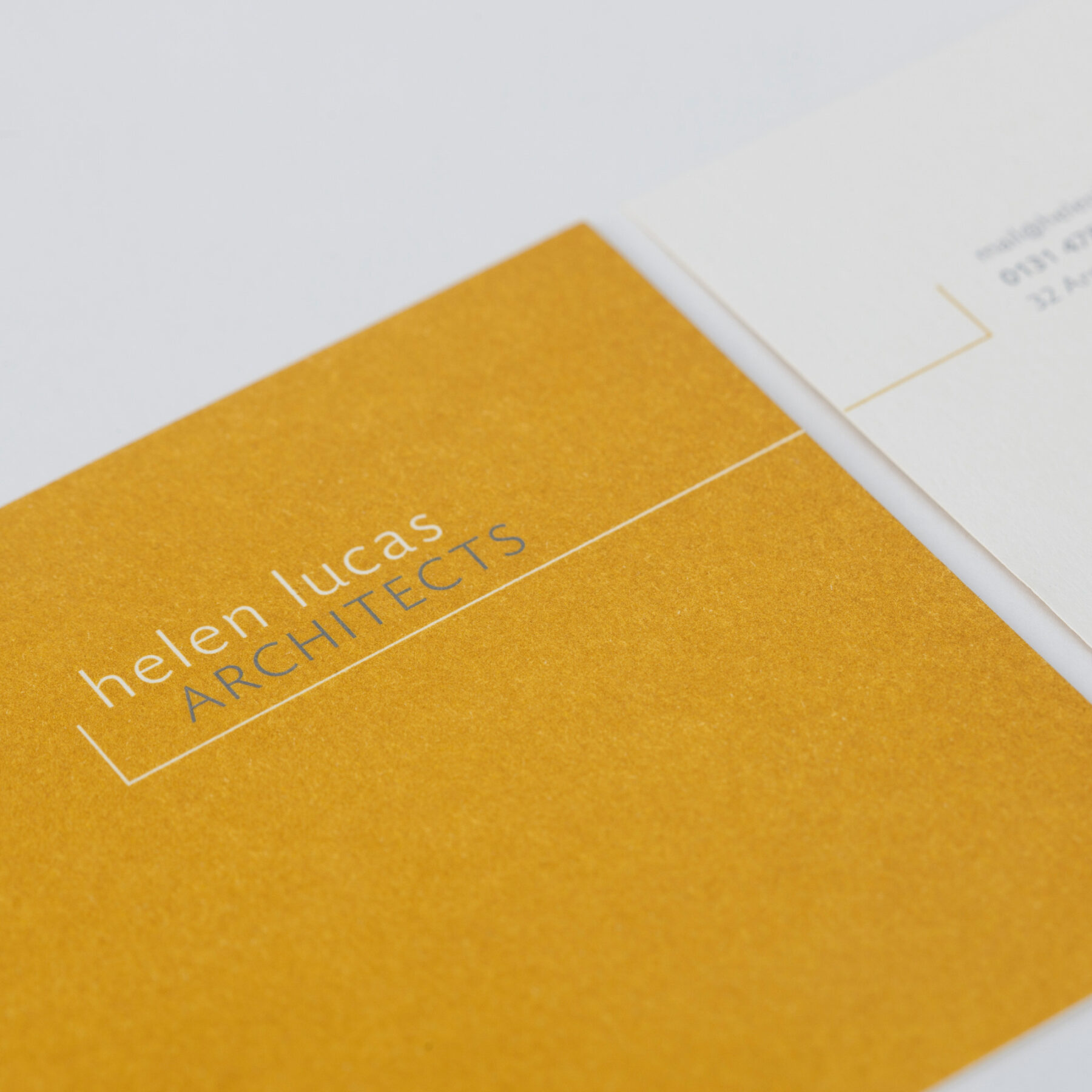 Close-up of Helen Lucas Architects yellow ochre postcard with white and grey logo.