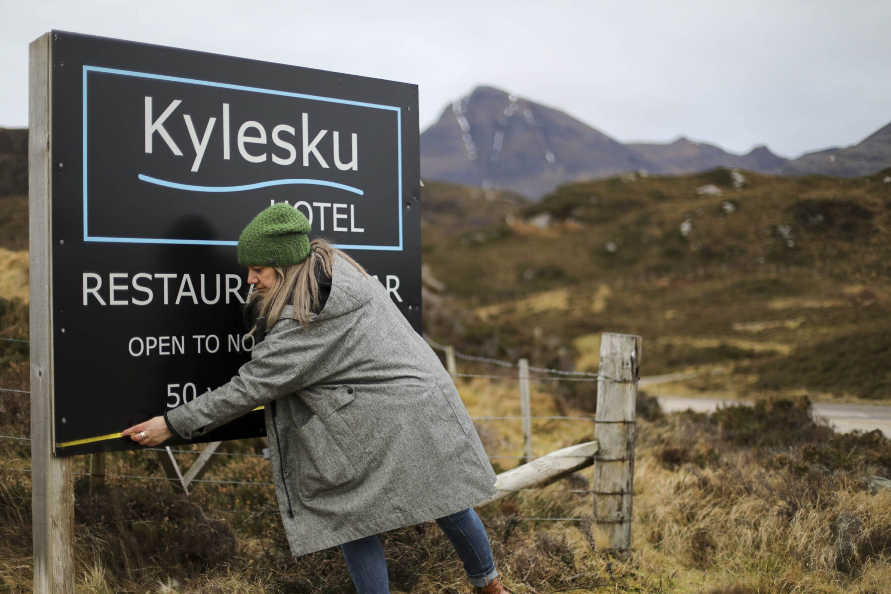 Measuring up the old Kylesku sign with landscape in the background.