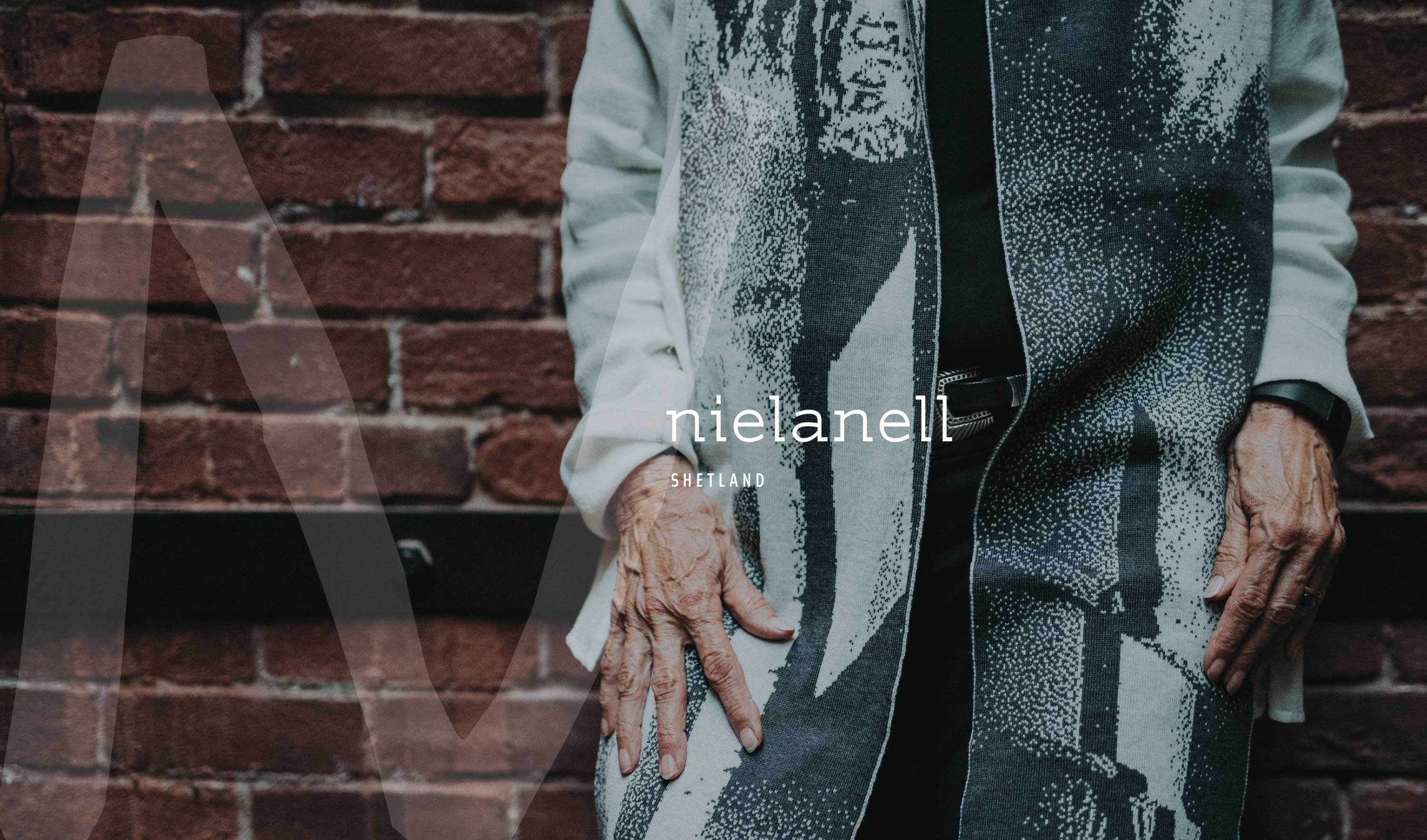 Model wearing Nielanell Byre scarf in front of brick wall with large Nielanell N overlaid.