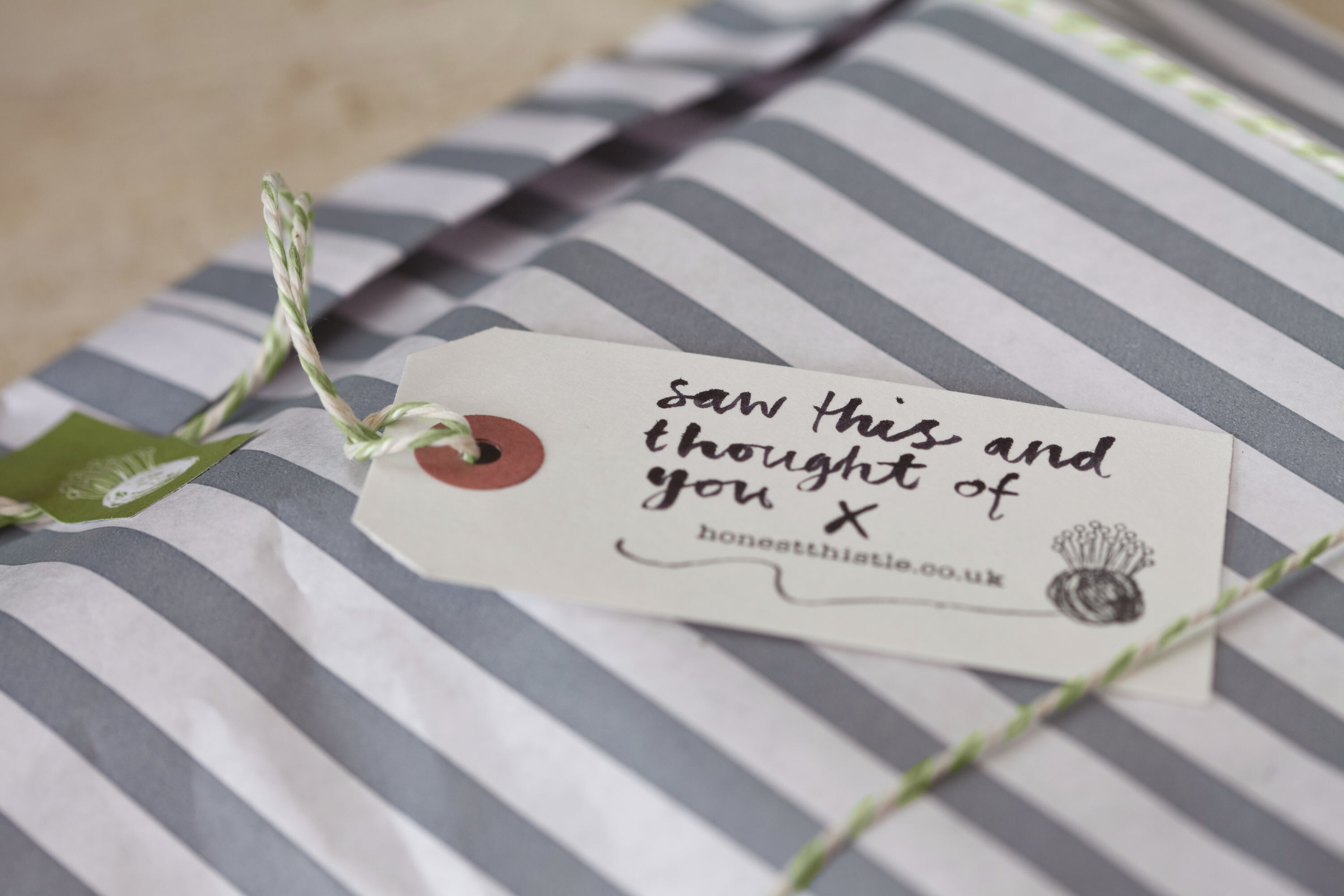 Grey and white striped paper bag with green and white striped string and cream tag. 'Saw this and thought of you' hand written on tag.